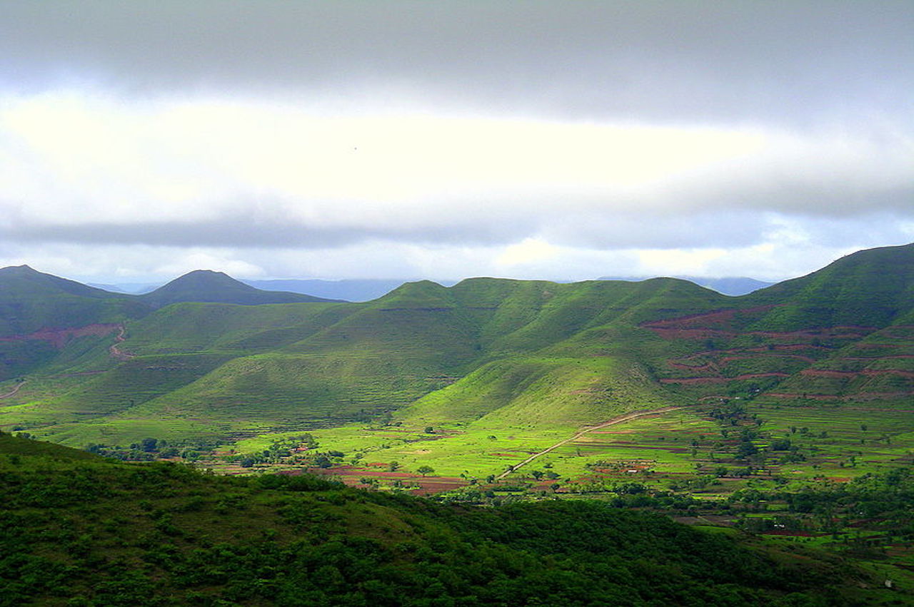 With grey cloud in sky in a monsoon season, the sun shines on the green mountains of western ghats