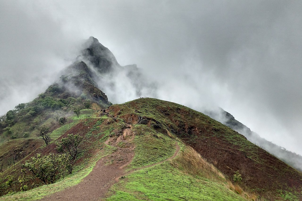 A trail passing through the mountain peak to the less visible mountain peak covered with grey fog on a monsoon season