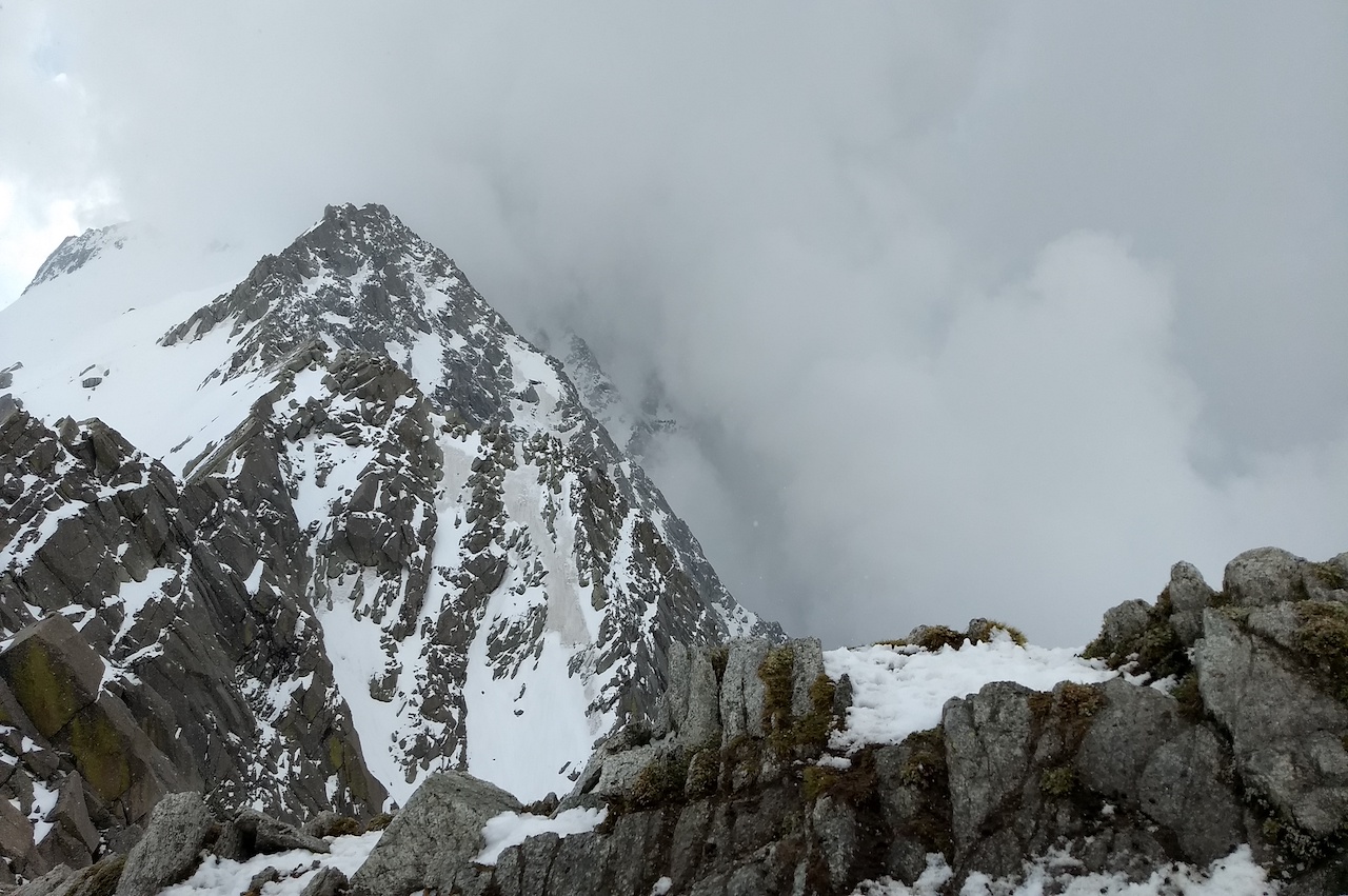 Ridge of a high altitude mountain with snow trails with big rock blocks surrounded by the grey fog like path to heaven