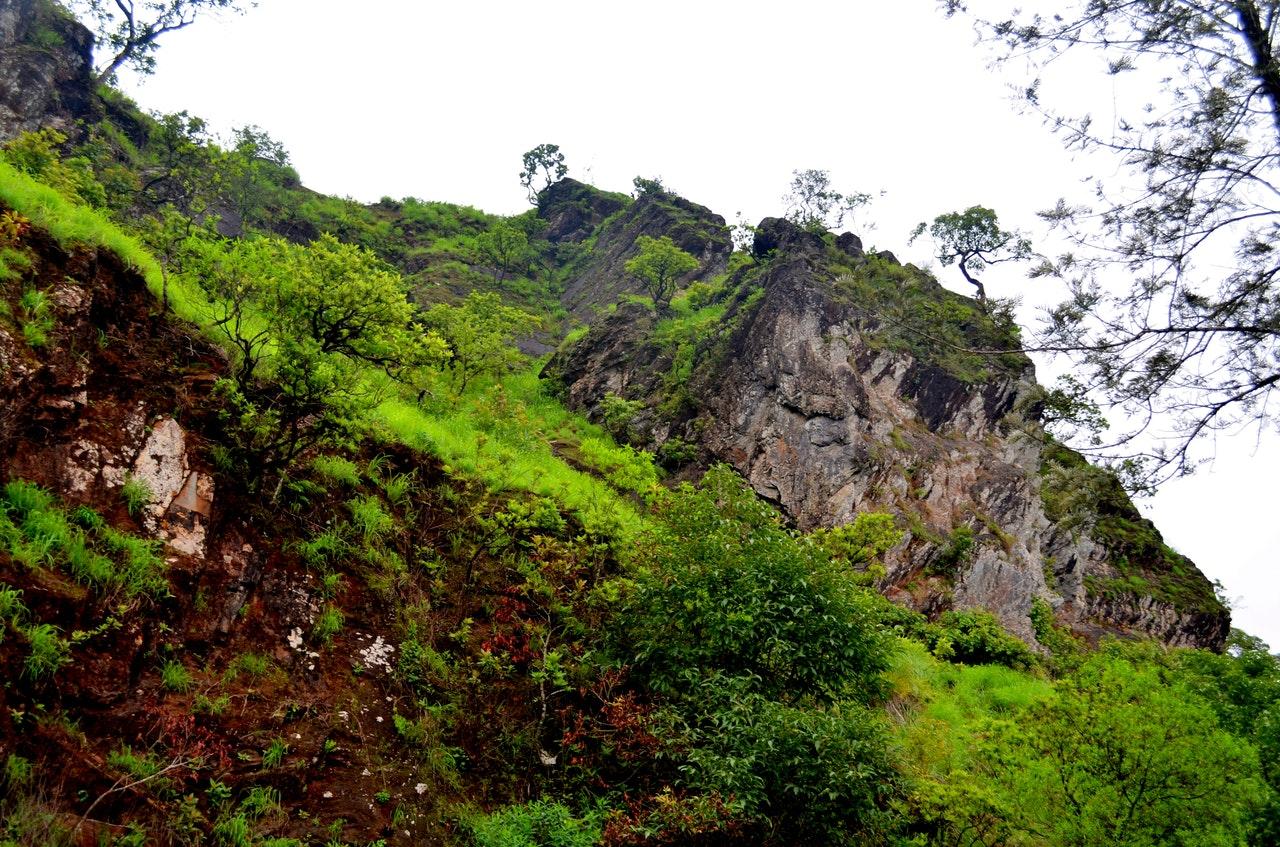 Huge block of rock in a mountain slope covered with green grass and trees on a sky full of grey cloud