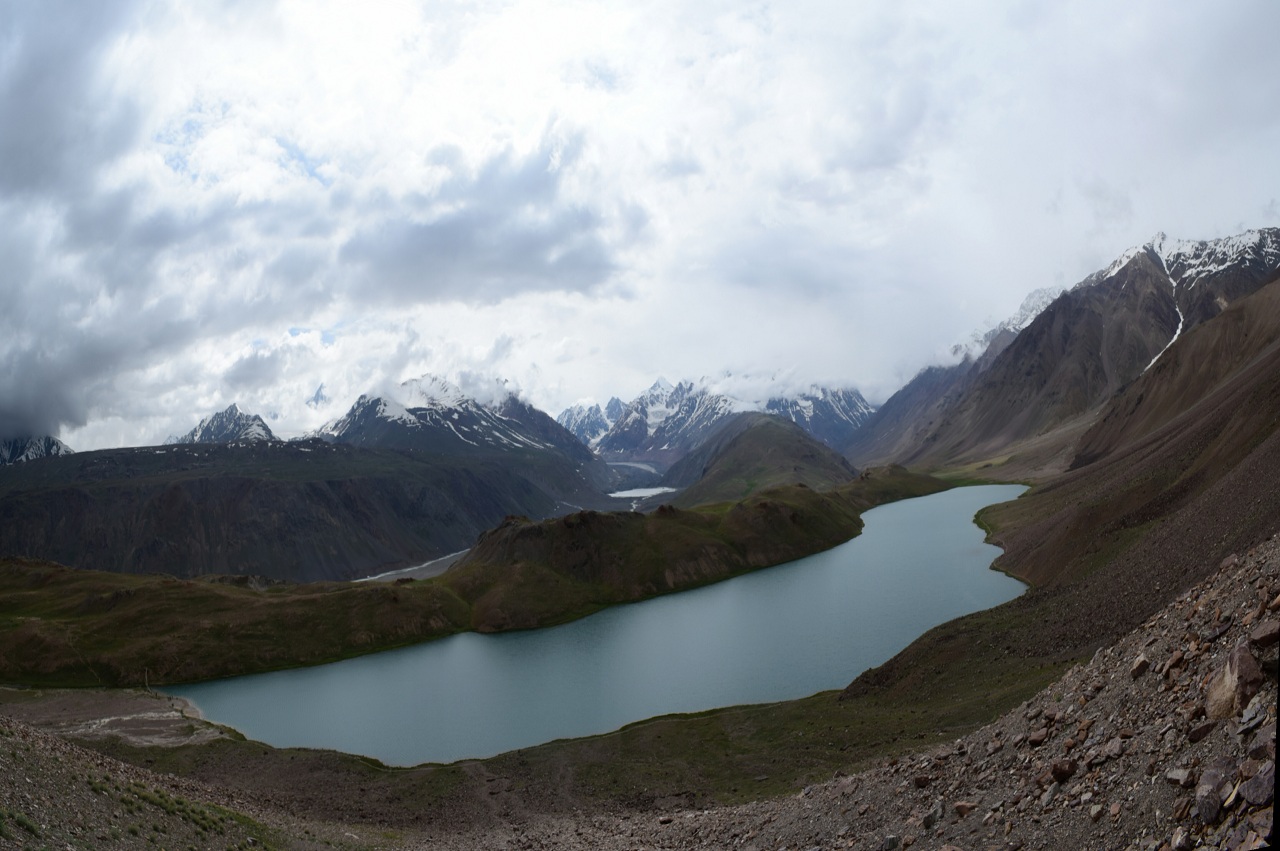 crescent shape chandratal lake with cloud covereing the top of mountains in the surrounding