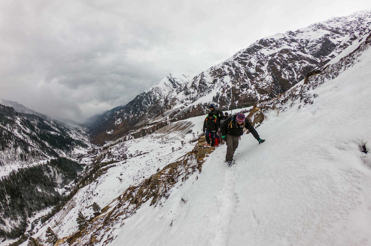 Trek leader making way for fellow trekkers in the Har ki dun valley through snow covered mountian with cloudy sky above