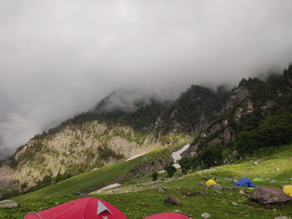 tents pitched on a plain ground in mountain slope with fog covering top of mountain peak