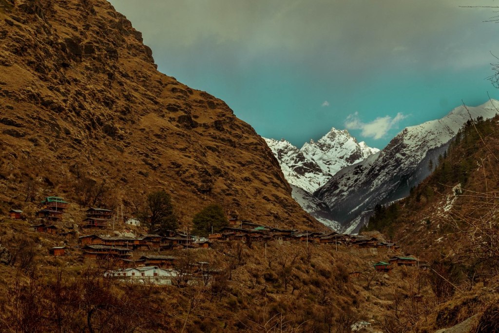 Gangad village lying on the slope of mountain with visible snow capped himalayan mountain on back