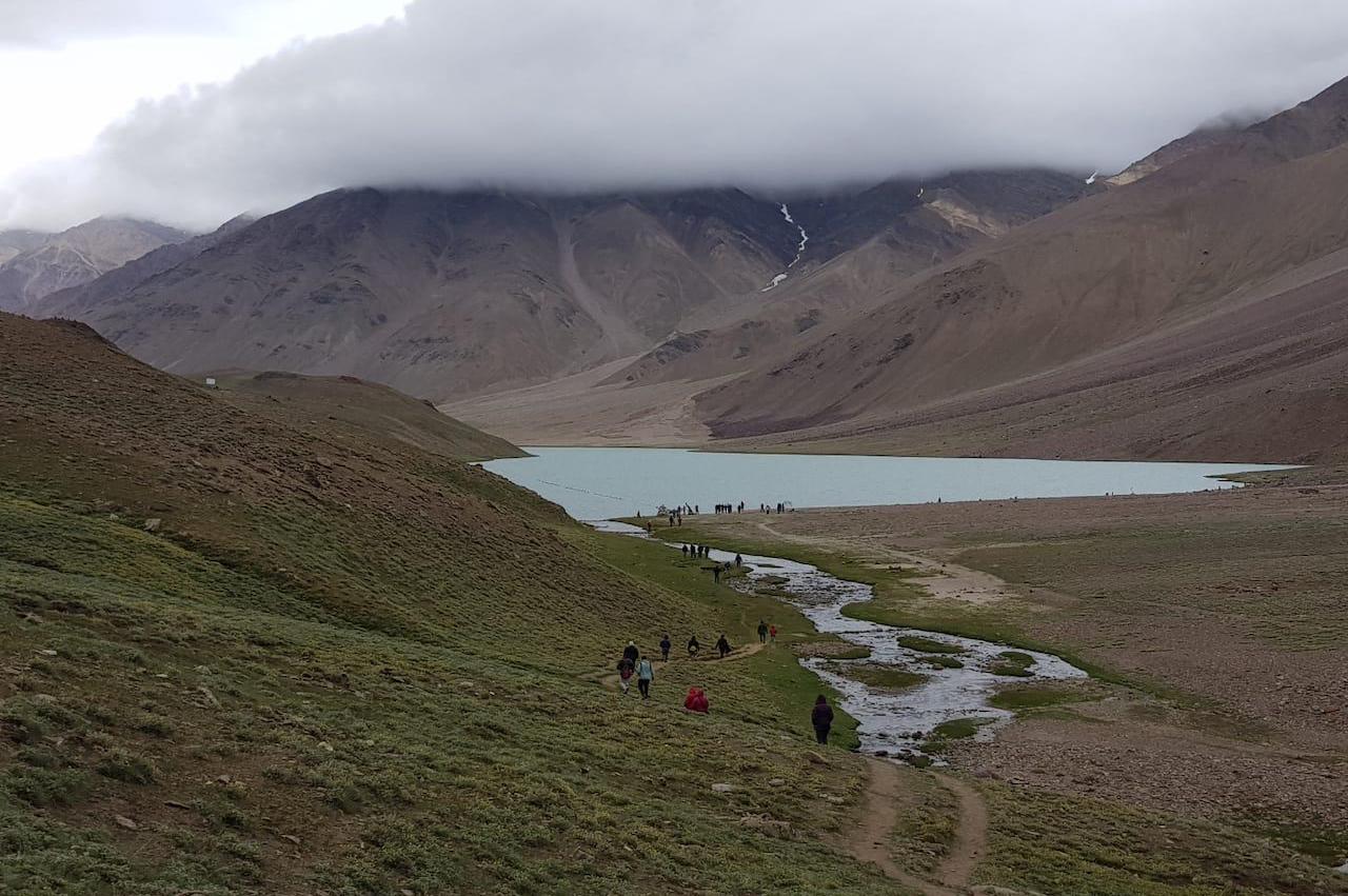 People walking toward the Chandratal lake through the single trail with Fog over the lake hiding the peak of mountain in front