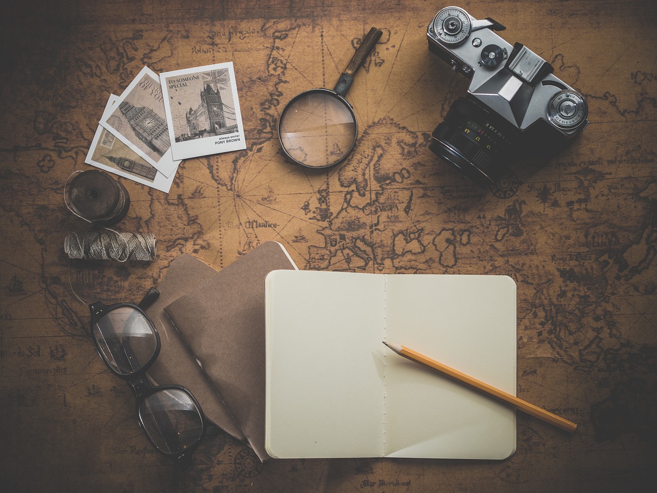 A notebook, pen, goggles, camera, magnifies, and a couple of stamp lying over world map