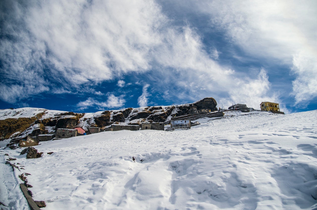 snow covering the ground in Tungnath with houses and tungnath temple on the way to chandrashila with couds shattering in the sky