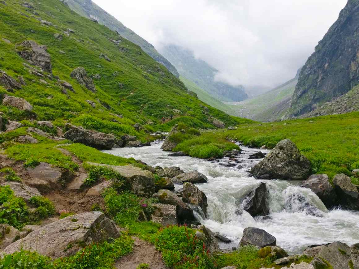 river flowing along the valley of lavish green mountains in hampta pass valley