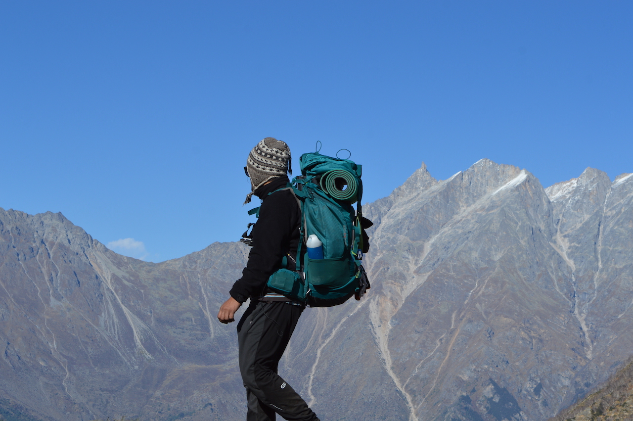 Man wearing black jacket carrying blue backpack going downhill in garhwal himalaya region